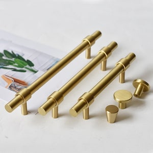 May include: A set of five gold-toned cabinet hardware pulls. Three are long, straight pulls with a cylindrical design. Two are smaller, round knobs.