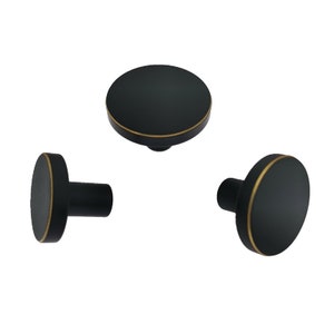 May include: Three black round cabinet knobs with a gold trim. The knobs have a small post on the back for mounting.