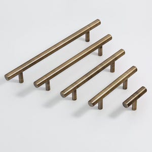 Op de afbeelding: Vijf geborstelde messing kastgrepen in verschillende lengtes. De grepen hebben een eenvoudig, recht ontwerp met afgeronde uiteinden.