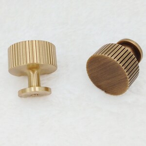 May include: Two gold-toned cabinet knobs with a ribbed design. The knobs have a round base and a cylindrical stem.