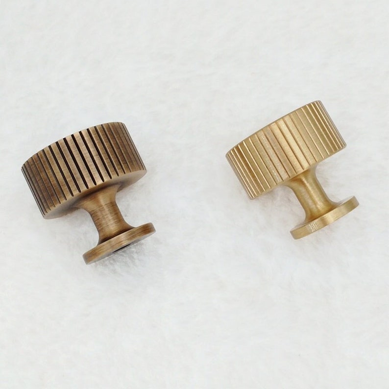 May include: Two brass cabinet knobs with a fluted design. The knobs have a round top and a cylindrical base.