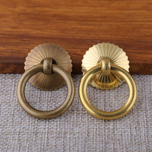 May include: Two antique brass cabinet door pulls with a ring handle and a decorative sunburst design.