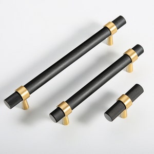 May include: Three black cabinet pulls with gold accents. The pulls are in different sizes and have a textured finish.