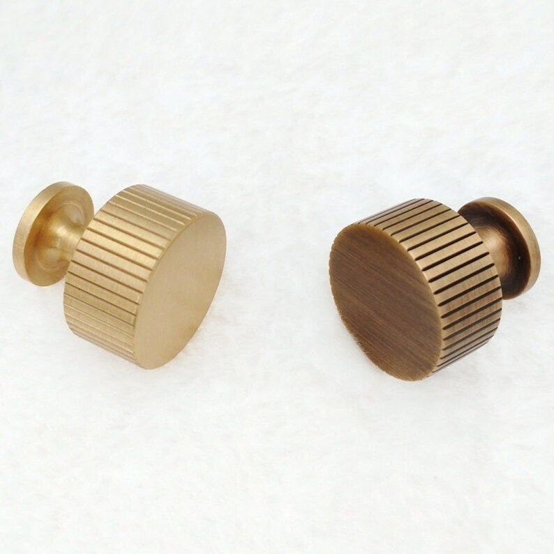 May include: Two brass cabinet knobs with a ribbed design. The knobs are round and have a smooth, polished finish.