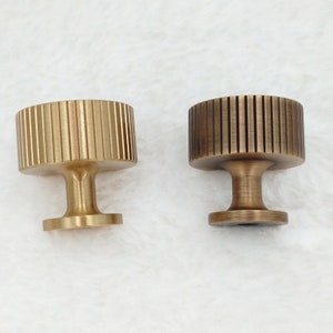 May include: Two brass cabinet knobs with a fluted design. The knob on the left is a polished brass finish, while the knob on the right is an antique brass finish.