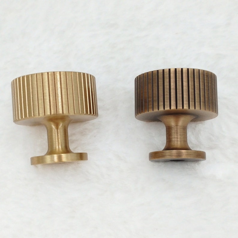 May include: Two brass cabinet knobs with a fluted design. The knob on the left is a polished brass finish, while the knob on the right is an antique brass finish.
