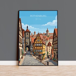 May include: A framed art print of Rothenburg, Germany, featuring a cobblestone street lined with colorful buildings. The artwork has a blue sky with clouds and the text "Rothenburg Germany" at the top.