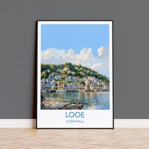 May include: A framed art print featuring a coastal town scene. The artwork depicts a hillside dotted with buildings, a harbor with boats, and the text "LOOE CORNWALL" at the bottom. The sky is blue with fluffy white clouds.