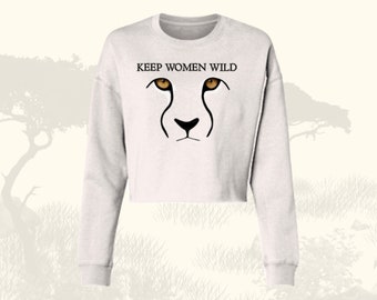 May include: A white cropped sweatshirt with long sleeves featuring a black cheetah face with orange eyes and the text "KEEP WOMEN WILD" printed on the front.
