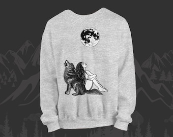 May include: Light gray sweatshirt featuring a black and white illustration of a wolf howling at the moon, with a woman sitting nearby. The moon graphic is above the woman and wolf. The sweatshirt has a crew neck and long sleeves.