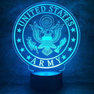 Könnte beinhalten: Ein blaues Acryl-Nachtlicht in Form des Siegels der US-Armee. Das Siegel zeigt einen Adler mit einem Schild und Olivenzweigen, umgeben von Sternen und den Worten "United States Army".