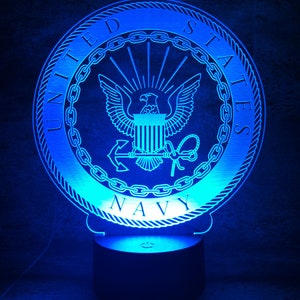 Peut inclure: Une veilleuse bleue en impression 3D en forme de sceau de la marine américaine. Le sceau représente un aigle avec un bouclier, une ancre et les mots "United States Navy".