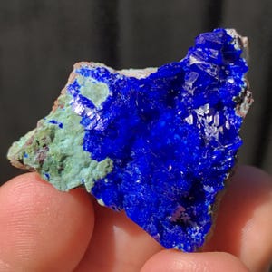 May include: A close-up of a blue and green mineral specimen. The mineral has a rough, textured surface and is covered in small crystals. The blue crystals are more prominent and have a deep, rich color.