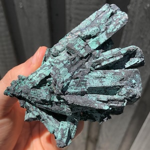 Könnte beinhalten: Ein Cluster aus schwarzen und grünen Azurite-Kristallen mit einer rauen, strukturierten Oberfläche.