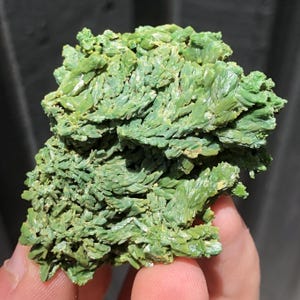 Puede incluir: Primer plano de un vibrante espécimen mineral verde. El mineral tiene una estructura cristalina con una apariencia en capas y texturizada. El color es un verde brillante y consistente, con algunas áreas que aparecen ligeramente más claras.