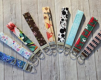 May include: A collection of ten colorful fabric keychains with metal key rings. The keychains feature various patterns, including floral, geometric, and cartoon characters.