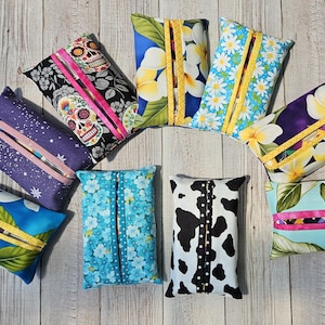 May include: Nine different fabric tissue box covers. The covers are made of various colorful fabrics with different patterns, including floral, skull, and cow print.