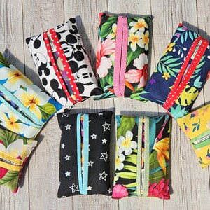 May include: Eight different tissue box covers with various patterns. The patterns include floral, tropical, Mickey Mouse, stars, and geometric designs. The covers are made of fabric and have a zipper closure.