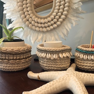May include: Three crocheted baskets with white shells and beads. The baskets are on a wooden surface with a white starfish. The baskets are decorated with gold beads, turquoise beads, and white shells.