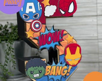 May include: A colourful wooden number five decorated with superhero characters, including Captain America, Spiderman, Iron Man, and Hulk. The number has a red, yellow, and blue colour scheme with the words "WOW!" and "BANG!" in comic book style.