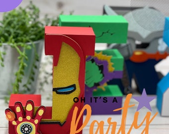 May include: A red, yellow, and blue cardboard letter J decorated with an Iron Man design. The letter is part of a set of letters that spell "Party" with the text "Oh it's a" below the letters. The letters are on a wooden surface.