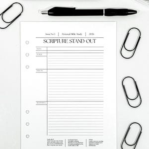 May include: A white personal Bible study sheet with the text "SCRIPTURE STAND OUT" and the year 2026. The sheet is accompanied by black pens and paper clips. The sheet has sections for date, verse, focus, and response.
