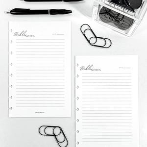 Può includere: Un set di cancelleria con due penne nere, due pagine bianche a righe "Bible Notes", graffette nere e un contenitore trasparente pieno di oggetti circolari neri. Le pagine presentano il testo "Bible Notes".