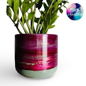 May include: A cylindrical plant pot featuring a vibrant magenta and deep purple abstract ink wash design on the upper portion, transitioning to a solid light grey base. A green ZZ plant grows from the pot, and a circular logo reads rrart creation.