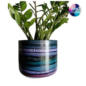 May include: A cylindrical plant pot featuring horizontal bands of deep blue, teal, purple, and black with speckled white accents. A green Zamioculcas plant grows from the top. A circular logo in the top right corner displays the text rrart creation.