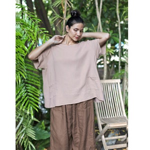 May include: A loose-fitting, light brown, short-sleeved top with a scoop neck and a patch pocket on the left side. The top is made of a soft, textured fabric and is paired with brown pants.