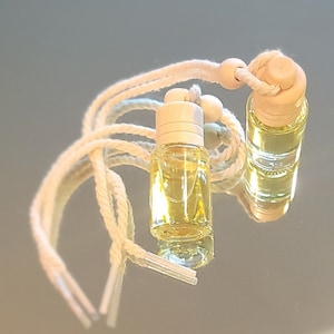 May include: Two small glass bottles with a yellow liquid inside, hanging from a white string with wooden beads. The bottles have white caps and are attached to a white string with wooden beads.