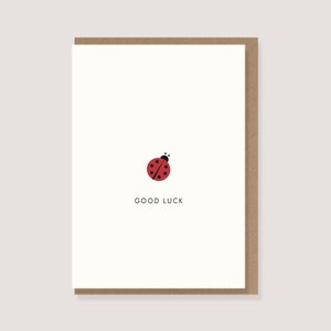 Könnte beinhalten: Eine weiße Karte mit einer roten Marienkäfer-Illustration und dem Text "GOOD LUCK" in Schwarz.