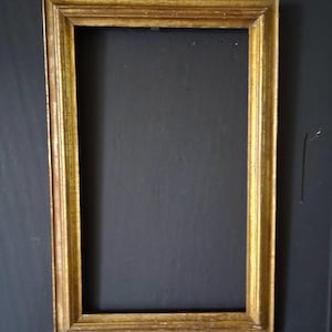 May include: A rectangular picture frame with a distressed gold finish and a stepped profile. The frame features a thin yellow string attached to the top center for hanging, showcasing a weathered texture with visible signs of age and wear.
