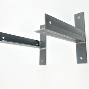 Könnte beinhalten: Zwei Metall-Regalböcke, einer über dem anderen, mit mehreren Löchern zur Montage. Die Böcke sind aus dunkelgrauem Metall und haben ein schlichtes, industrielles Design.