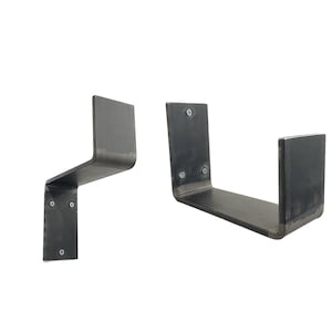 Może przedstawiać: Dwa metalowe wsporniki półki, jeden o prostym designie, a drugi o zakrzywionym designie. Oba wsporniki są czarne i mają surowy, industrialny wygląd.