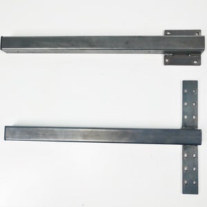May include: Two metal brackets with holes for mounting. The brackets are silver in colour and have a rectangular shape. The top bracket is straight, while the bottom bracket has a T-shape.