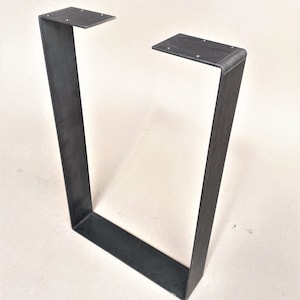 Puede incluir: Una pata de mesa rectangular de metal negro con un borde superior ligeramente redondeado.