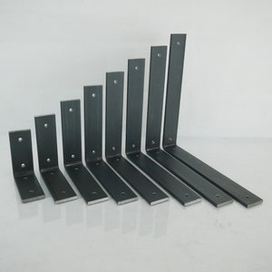 May include: A collection of eight dark gray metal shelf brackets of varying sizes. Each bracket has a right-angle design with pre-drilled holes for mounting. The brackets are arranged in a row, showcasing their different lengths and widths.