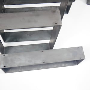 K&ouml;nnte beinhalten: Vier Metalltischbeine, die &uuml;bereinander gestapelt sind. Die Beine sind aus unbehandeltem Stahl und haben eine rechteckige Form.