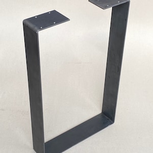 May include: A black metal table leg with a rectangular shape and a flat top. The leg is made of thick metal and has a simple, industrial design.