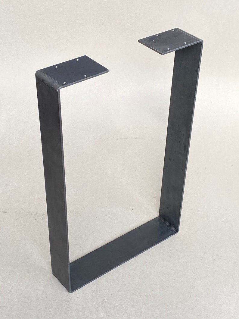 May include: A black metal table leg with a rectangular shape and a flat top. The leg is made of thick metal and has a simple, industrial design.