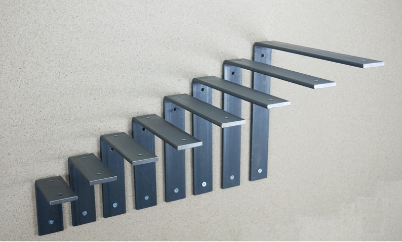 May include: A set of seven dark gray metal shelf brackets arranged in a descending staircase pattern. Each bracket is L-shaped with a flat top and a vertical support, secured to the wall with screws. The brackets are designed for supporting shelves.