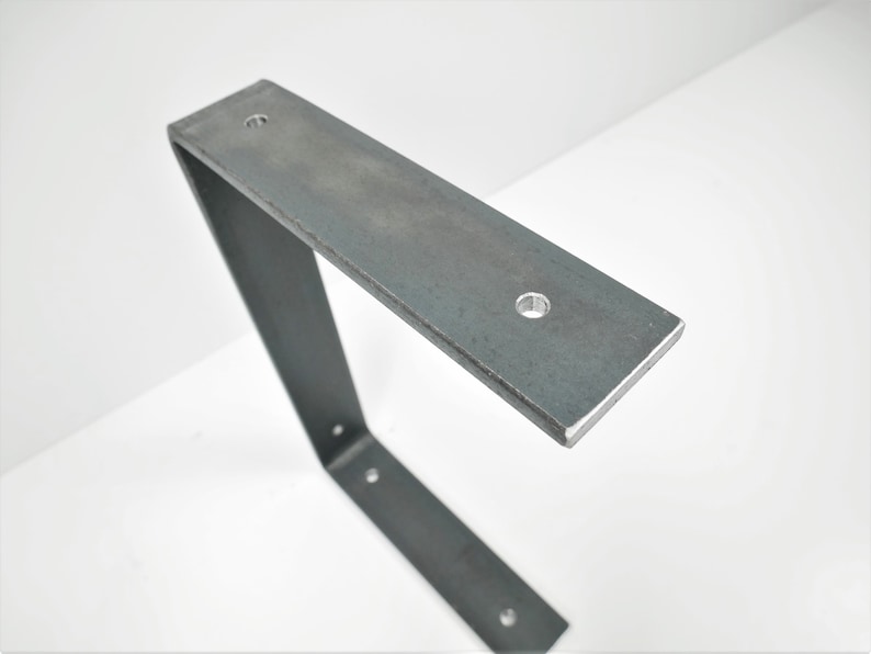K&ouml;nnte beinhalten: Eine Metall-Regalhalterung mit drei L&ouml;chern zur Montage. Die Halterung ist aus Stahl und hat eine rohe, unfertige Optik.