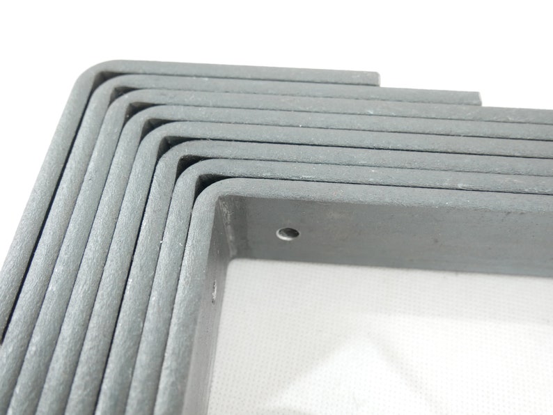 May include: A stack of gray, L-shaped corner brackets. Each bracket has a rounded corner and a pre-drilled hole. The brackets are made of a textured material and are stacked on top of each other.