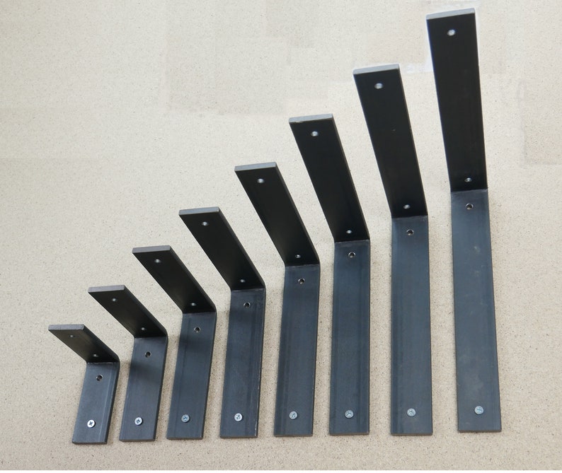May include: A set of eight black metal shelf brackets of varying sizes. Each bracket has a right-angle design with a vertical and horizontal section, and includes screw holes for mounting. The brackets are arranged in ascending order of size.