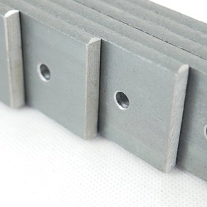 May include: Close-up of several gray metal plates with rounded corners and a centered hole. The plates are stacked, revealing their edges. The metal has a slightly rough texture.