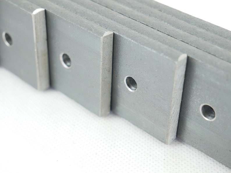 May include: Close-up of several gray metal plates with rounded corners and a centered hole. The plates are stacked, revealing their edges. The metal has a slightly rough texture.
