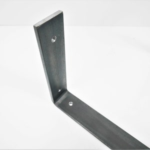 K&ouml;nnte beinhalten: Eine Metall-Regalhalterung mit drei L&ouml;chern zur Montage. Die Halterung ist aus rohem Stahl gefertigt und hat einen rustikalen, industriellen Look.