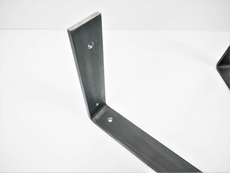 K&ouml;nnte beinhalten: Eine Metall-Regalhalterung mit drei L&ouml;chern zur Montage. Die Halterung ist aus rohem Stahl gefertigt und hat einen rustikalen, industriellen Look.