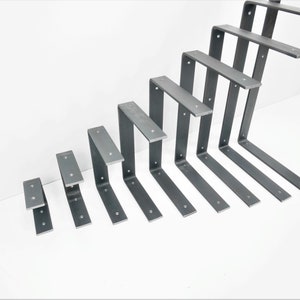 K&ouml;nnte beinhalten: Ein Satz von neun Metall-Regalb&ouml;cken in verschiedenen Gr&ouml;&szlig;en. Die B&ouml;cke sind aus Stahl und haben eine rohe, unfertige Optik. Sie sind in einem versetzten Muster angeordnet, wobei der gr&ouml;&szlig;te Bock oben und der kleinste Bock unten ist.